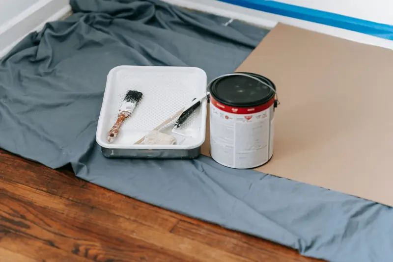 Pinceau, bac et pot de peinture sur une bâche qui protège le parquet
