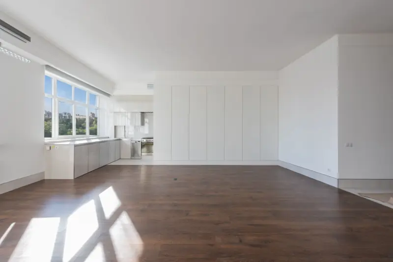 Séjour rénové au parquet en bois foncé, cuisine blanche ouverte au fond